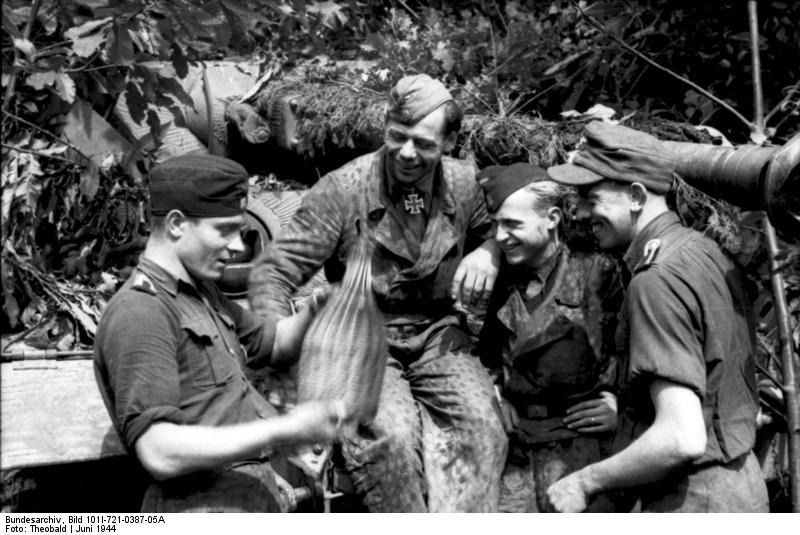 Members of the Waffen-SS in front of a camouflaged tank, France, June 1944